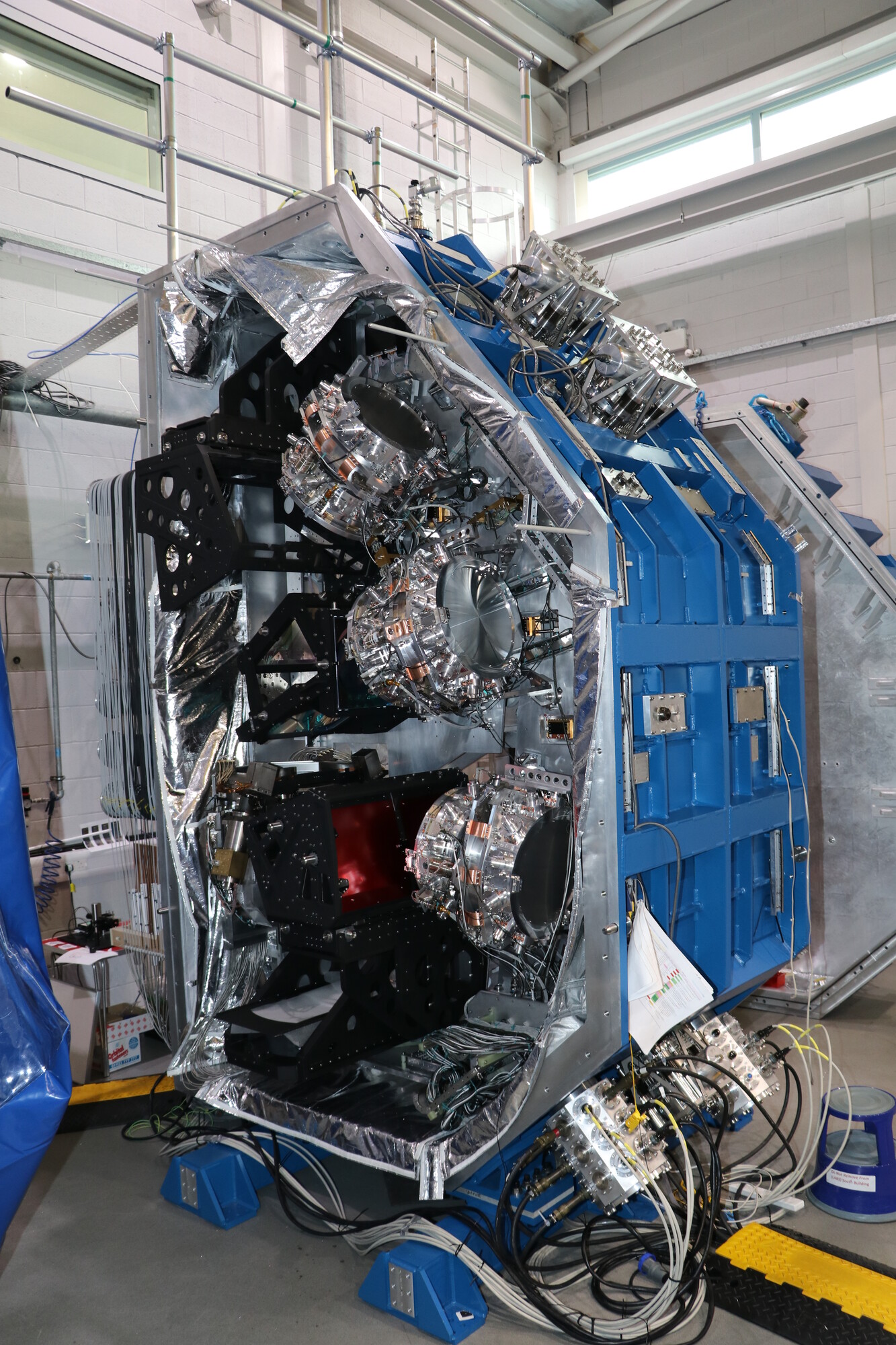 The MOONS instrument in the lab at the UK ATC. It looks like a large, blue metal box with cameras, wires and electronics inside.