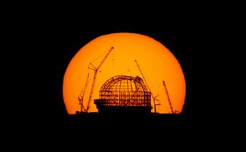 The construction of the Extremely Large Telescope seen in silhouette with the sun burning bright behind.